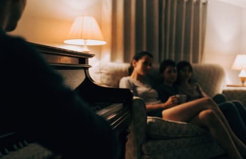 A family on a sofa in the evening, listening to someone play the piano